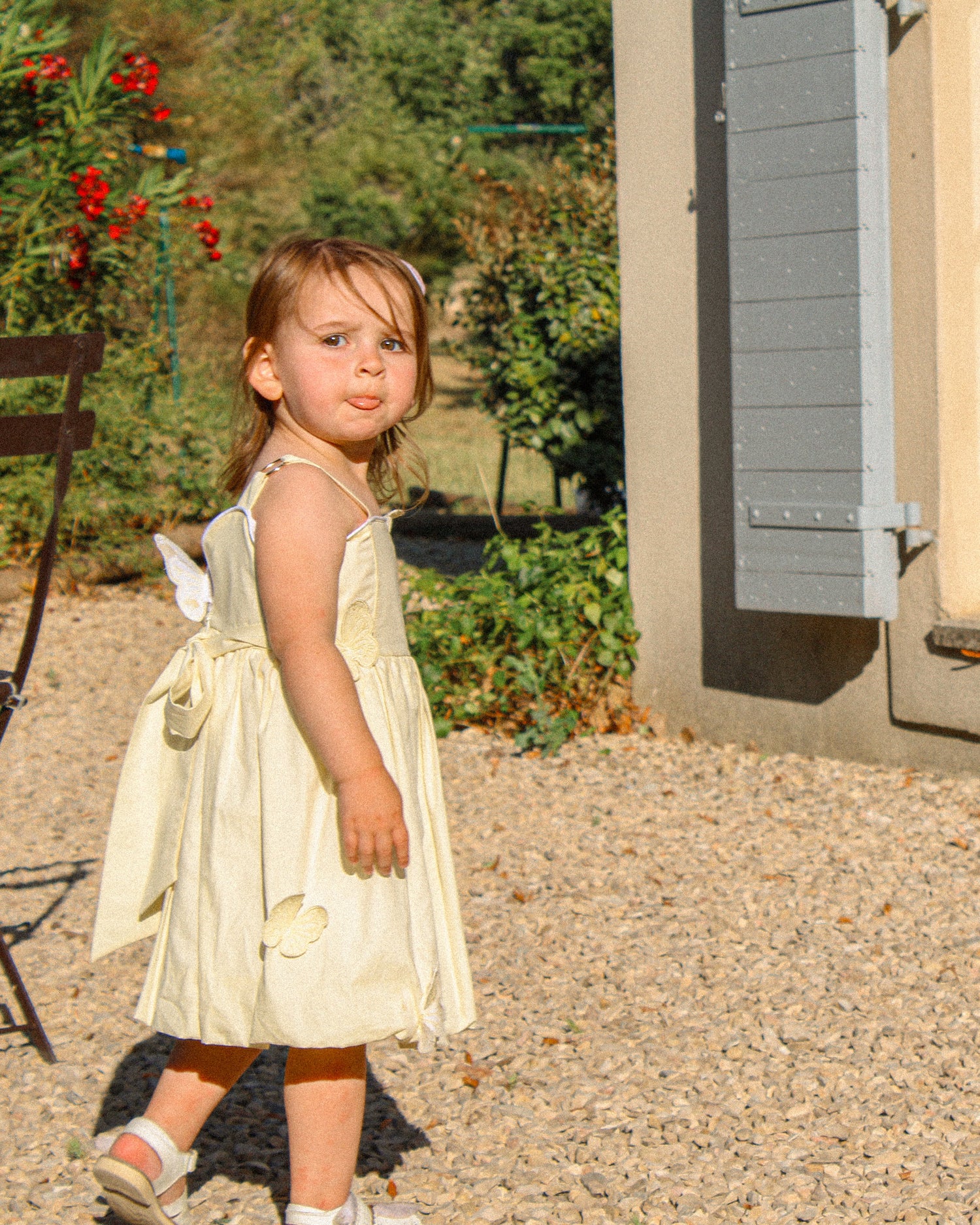 Young girl in a yellow dress standing in front of a house with a garden.