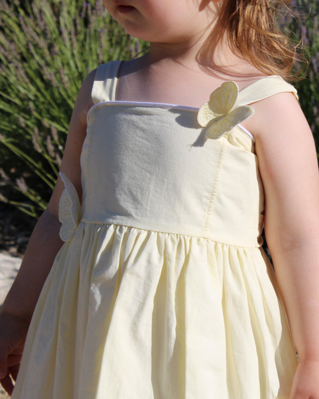 Child in a yellow organic birthday/ flower girl dress standing outdoors with greenery in the background
