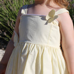 Child in a yellow organic birthday/ flower girl dress standing outdoors with greenery in the background
